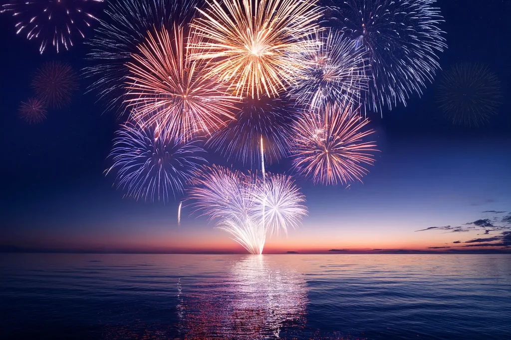 Colorful fireworks illuminate the ocean at sunset, creating a vibrant display over the water