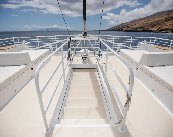 View from the deck of a yacht, featuring lounge beds and stairs leading down to the aqua blue ocean,