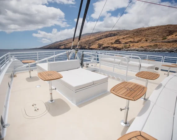 A spacious boat deck featuring a white cushioned seating area and wooden tables,