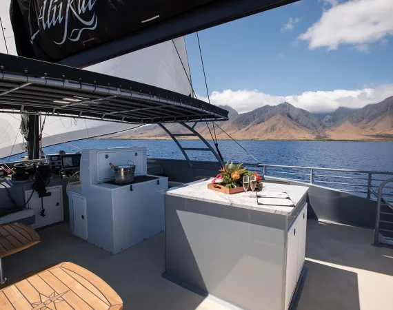 A luxurious boat deck featuring a marble table with a tropical floral arrangement, glasses, and an ice bucket, with scenic mountains in the background.