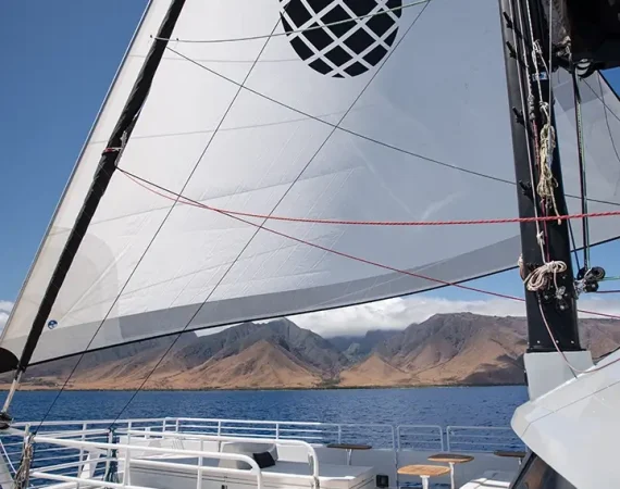Wooden tables on a yacht deck overlook the ocean, with white railings and a blue sky dotted with clouds in the background.