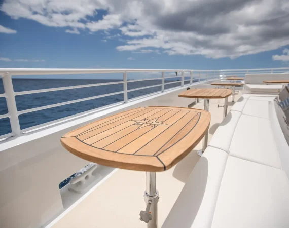 Wooden tables with a star design on a yacht deck, overlooking calm blue waters under a partly cloudy sky.