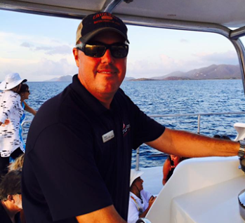 Man Steering A Boat On The Ocean With Mountains In The Background, Associated With Cruz Bay Watersports.