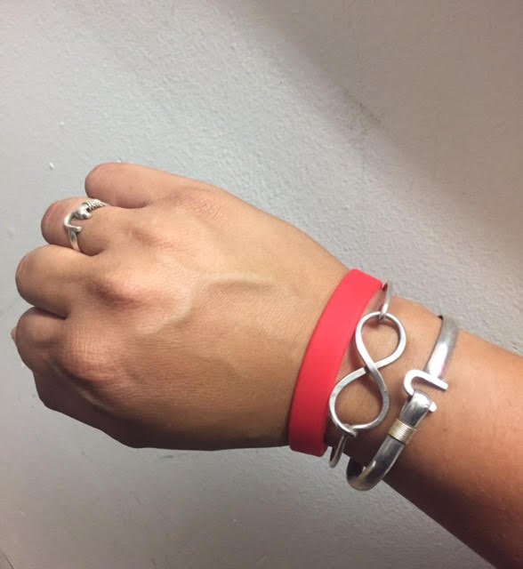 Hand Wearing A Silver Infinity Bracelet, Red Wristband, And A Ring, Showcasing Stylish Accessories.