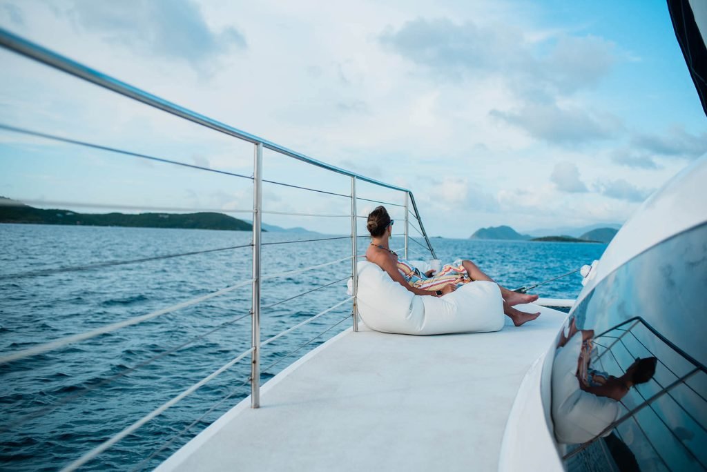 Woman Relaxing On White Yacht Bow Seating With Blue Ocean And Tropical Islands Under Cloudy Sky.