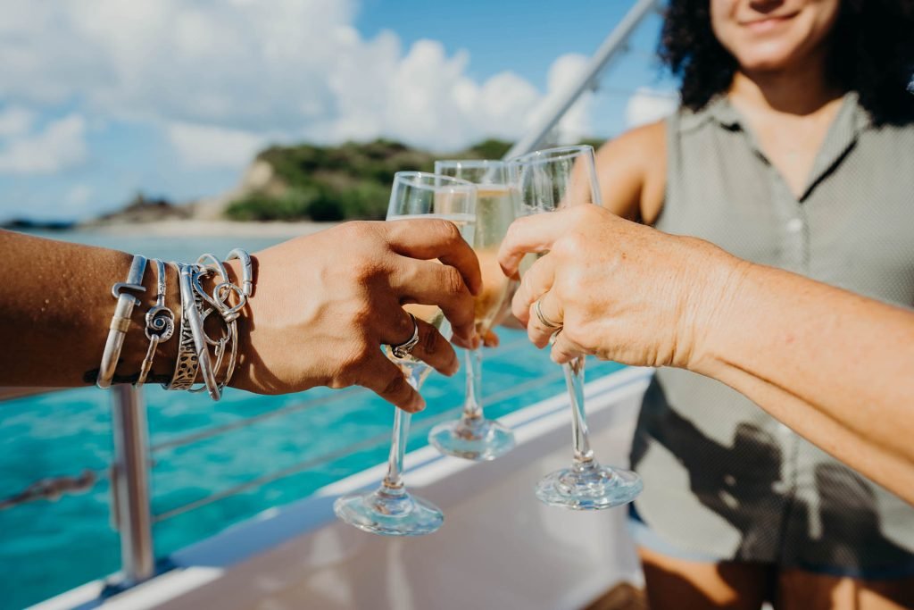 People Toasting With Champagne Glasses On Boat Deck With Turquoise Water And Tropical Islands.