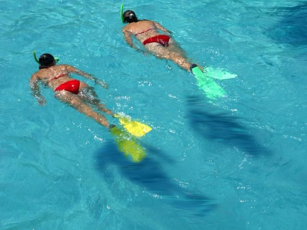 Two people snorkeling with fins in clear blue water, showcasing Cruz Bay watersports activities.