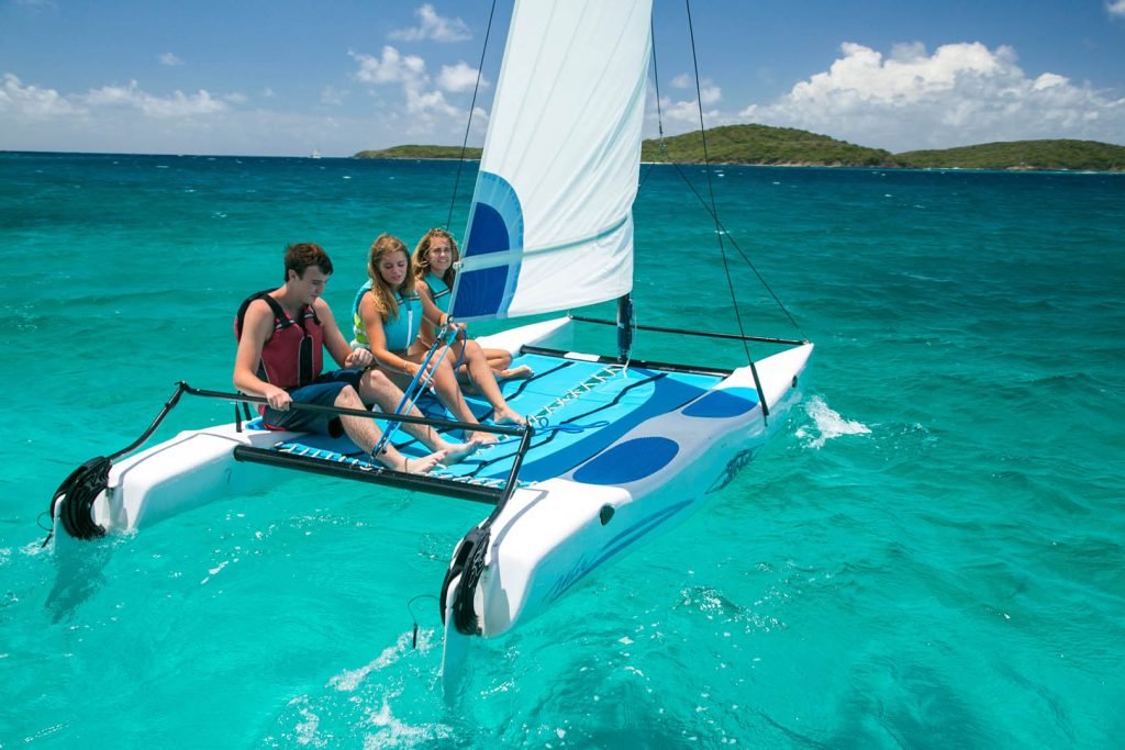 Group Of People Sailing On A Catamaran In Vibrant Turquoise Ocean Waters Under A Clear Blue Sky.