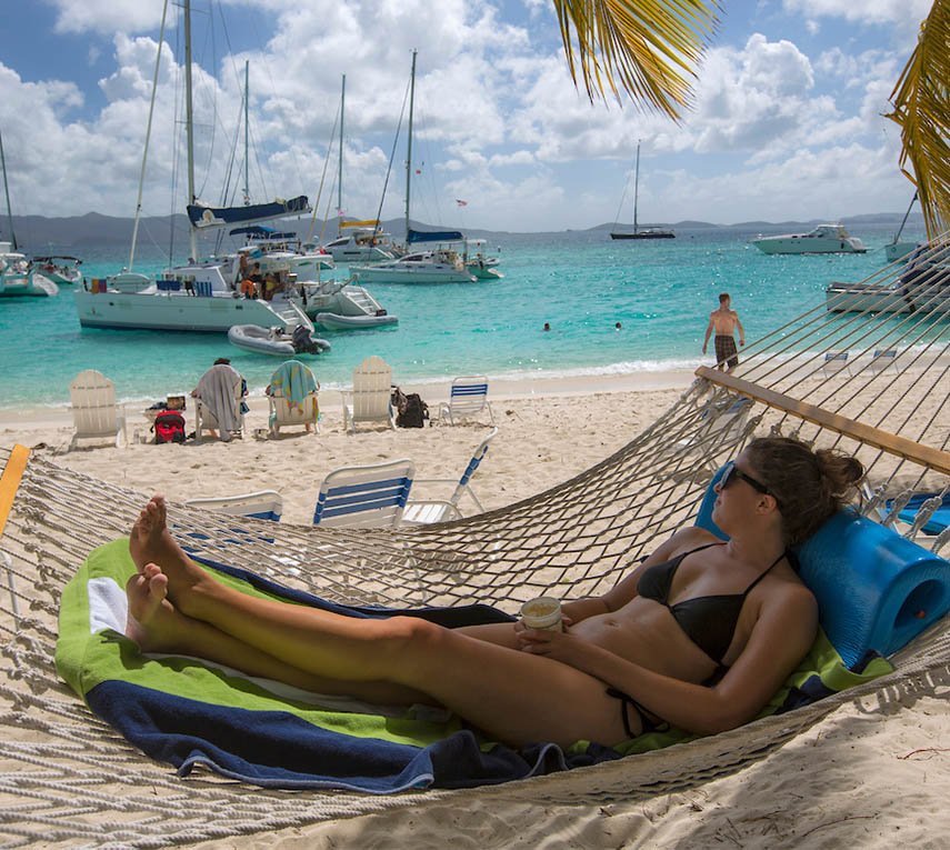 Woman relaxing in a hammock on a beach near Cruz Bay, with boats anchored in the turquoise waters.