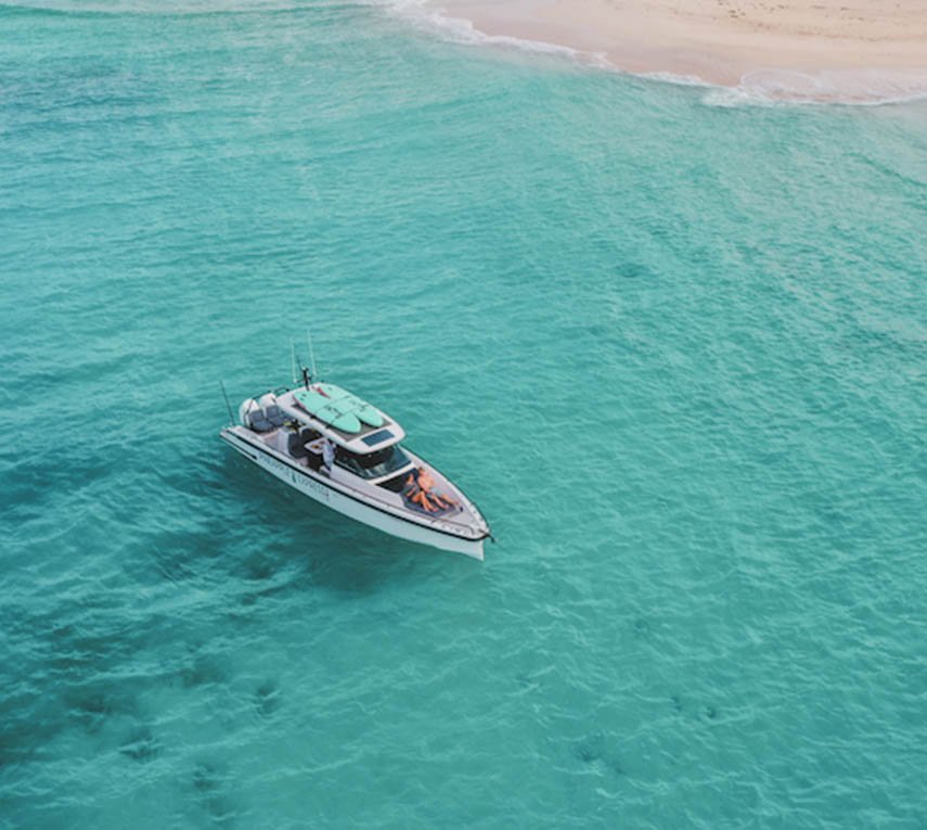 Aerial view of a speedboat on clear turquoise waters near a sandy beach.