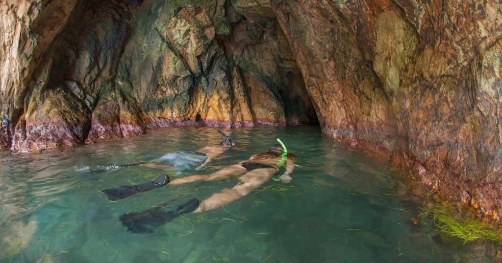 Snorkelers Exploring An Underwater Cave With Colorful Rock Formations.