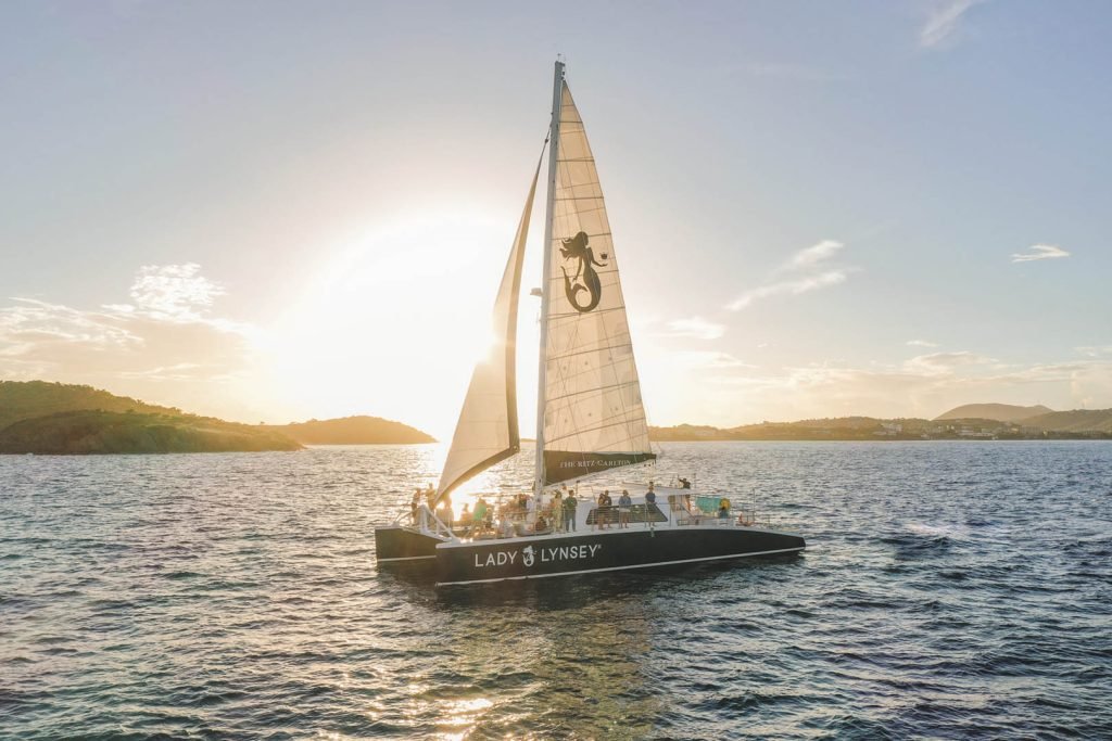 Catamaran Sailing At Sunset With Passengers, Island Backdrop, Luxury Travel Experience.