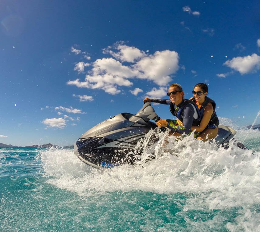 Two people on a jet ski making waves in sunny weather.