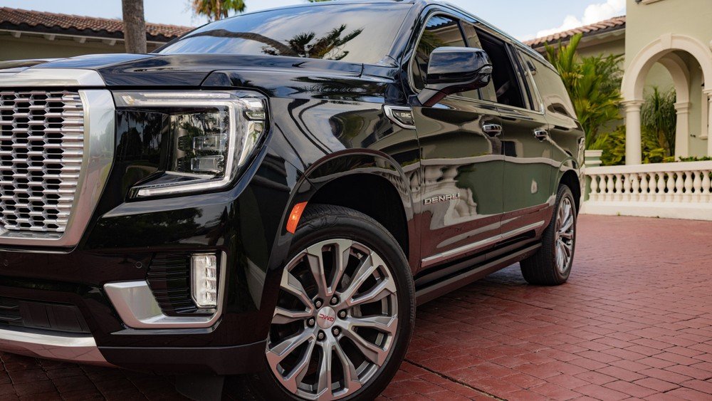 A Black Suv Parked In A Driveway With A Villa And Palm Trees In The Background.