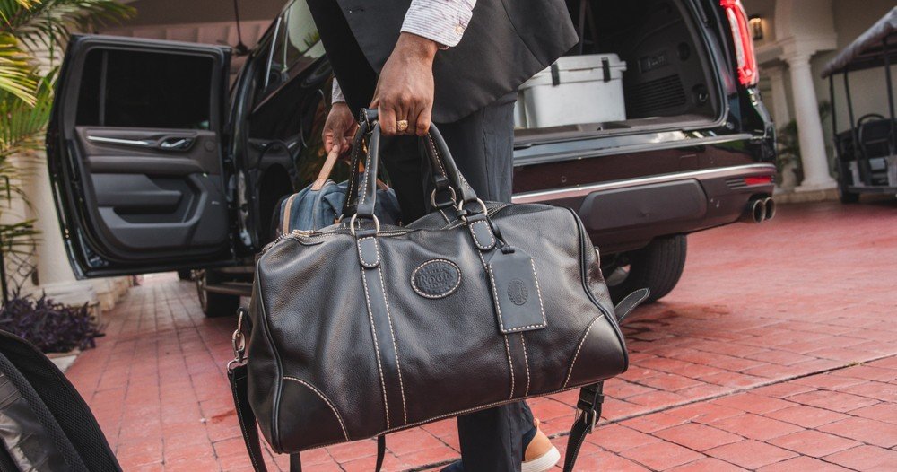 Man In Suit Carrying A Leather Bag Beside An Open Car Door.