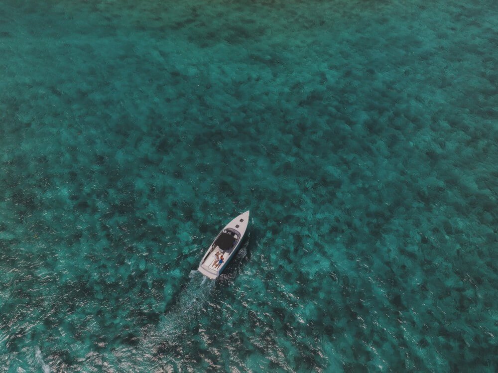 Aerial View Of A Small Boat Sailing On A Vast, Clear Blue Ocean.
