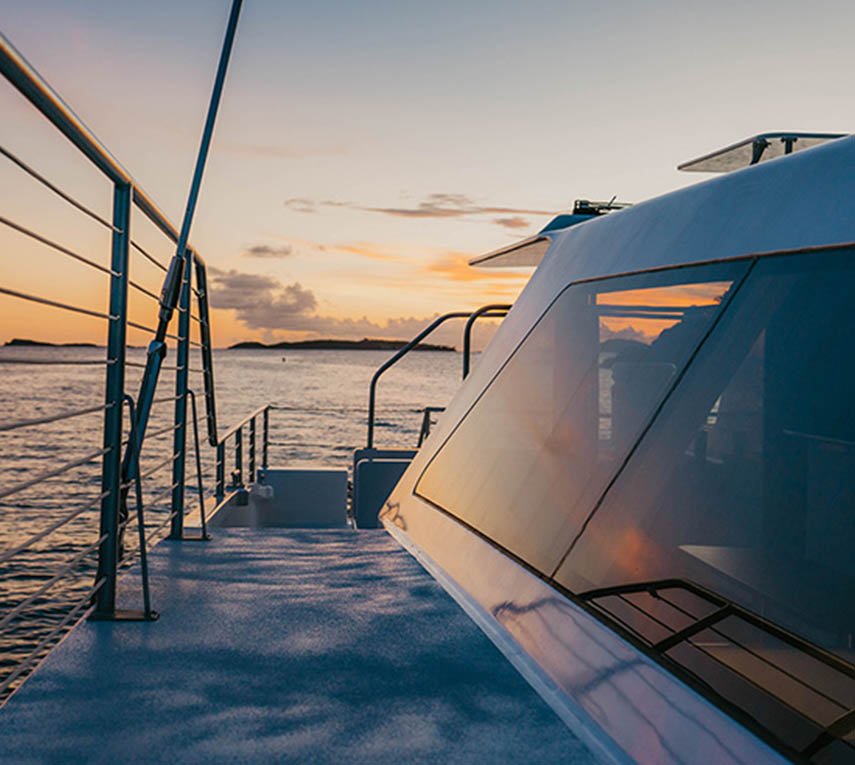 Sunset view from the deck of a yacht with reflective windows, calm sea and cloudy sky.