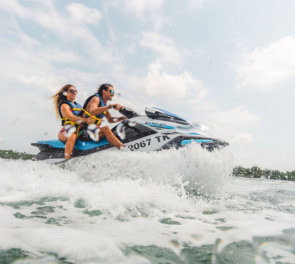 Two people riding a jet ski on the ocean, enjoying a sunny day with splashing waves.