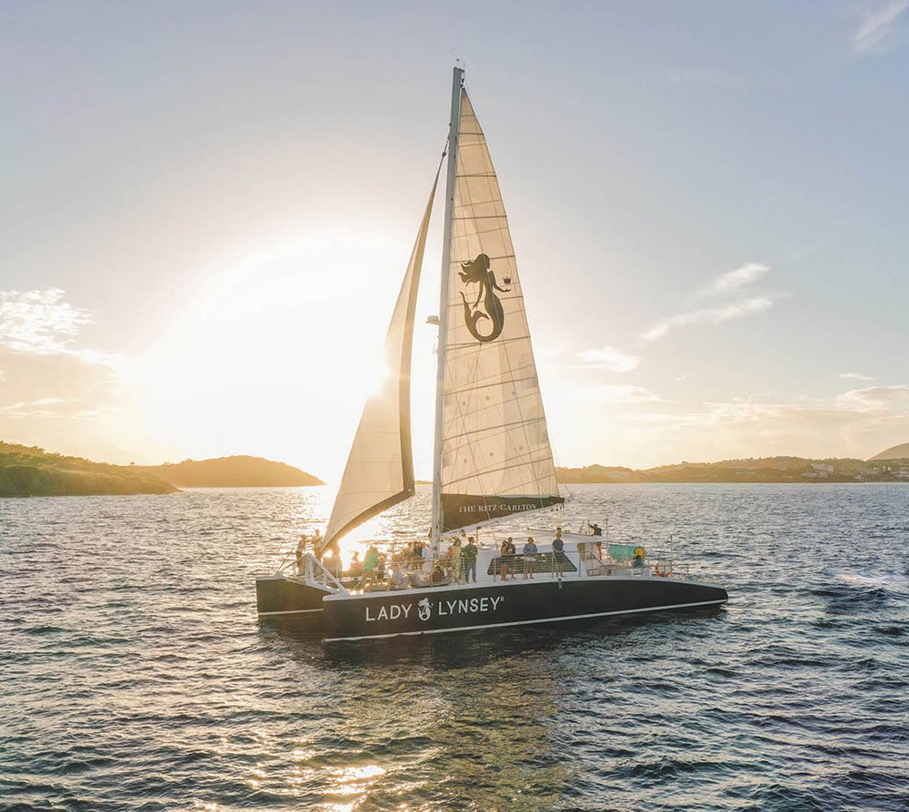 Sailboat "Lady Lynsey" on the ocean at sunset with a silhouetted mermaid design on the sail.