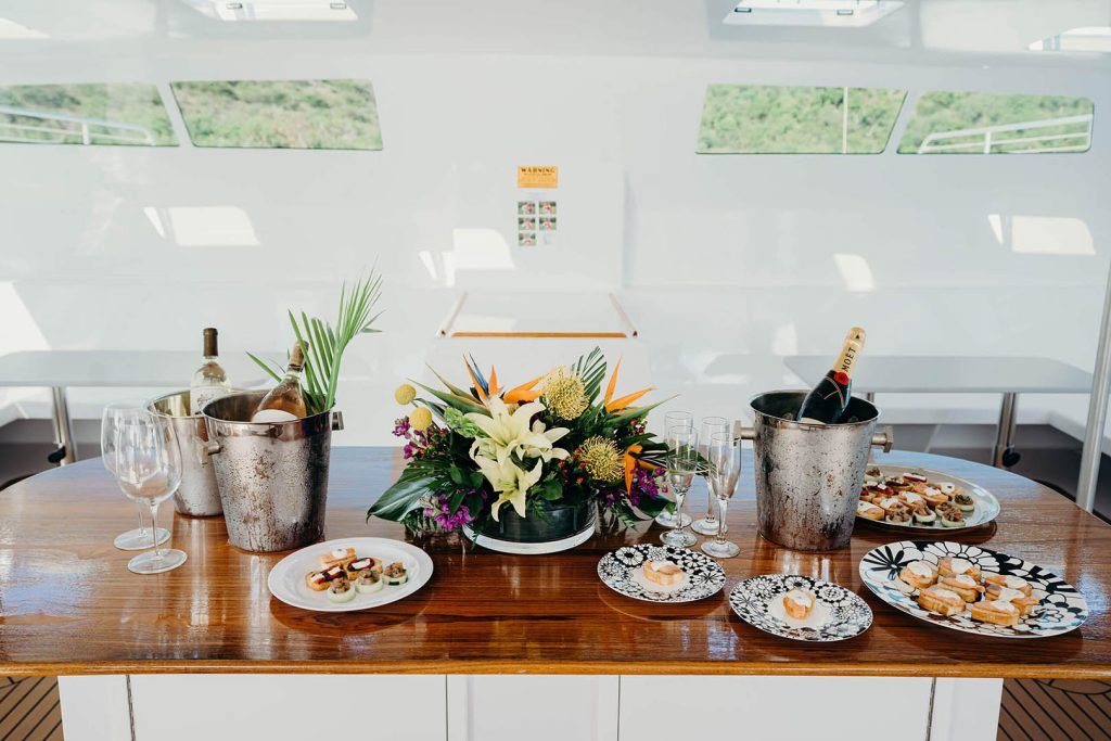 Champagne Bottle In Ice Bucket, Floral Arrangement, And Appetizers On Plates.