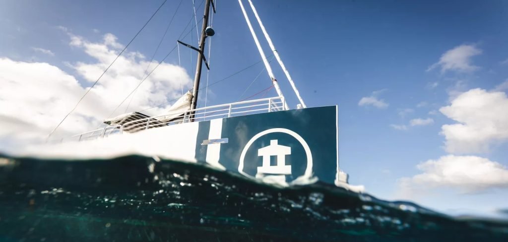 Partial underwater view of a sailboat showing its hull and mast under a clear blue sky.