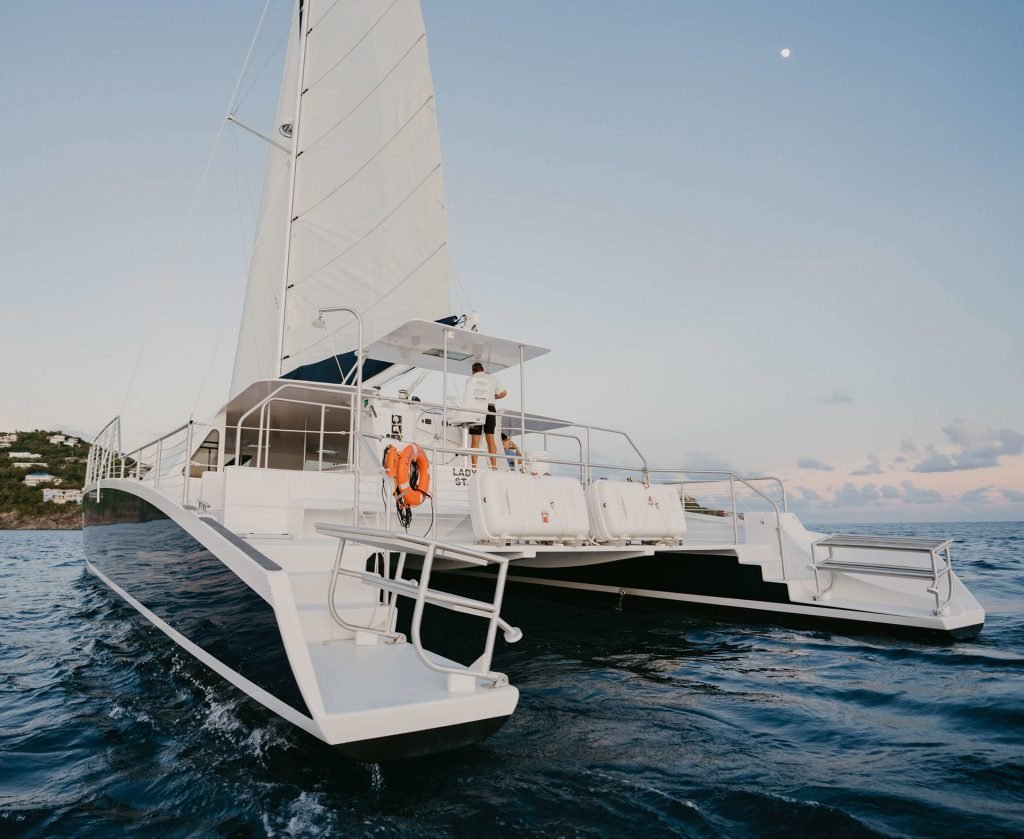 Sailboat Cruising Under A Vibrant Sunset In The Caribbean, Reflecting Golden Hues On The Water