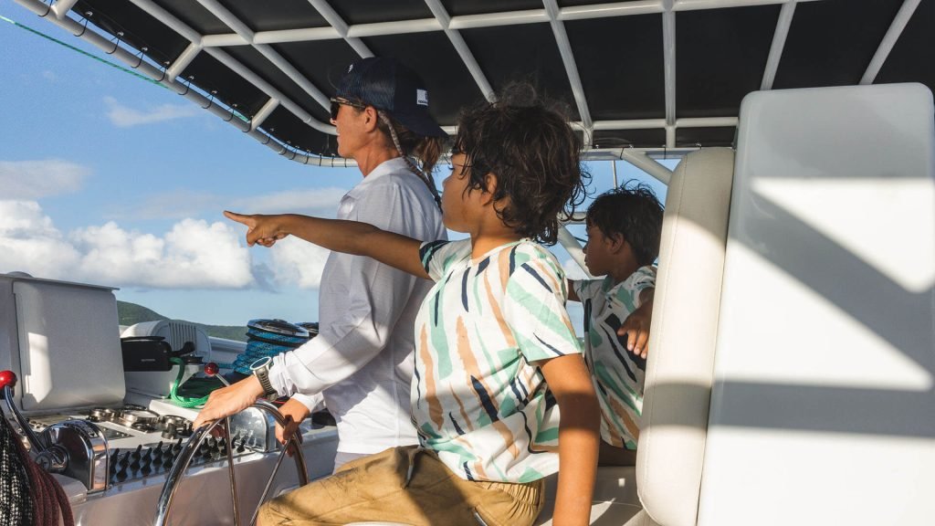 A family enjoying a boat ride, with a child pointing out towards the ocean while the adult steers the boat under a sunny sky.