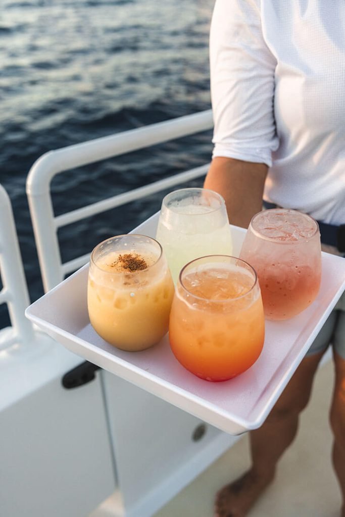 A tray of colorful cocktails being served on a boat, with ocean water in the background.