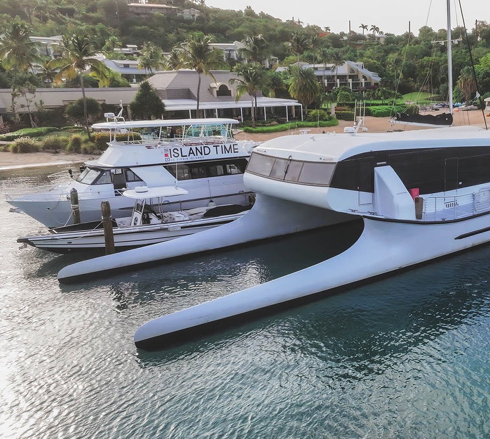 White catamaran and "Island Time" boat moored at tropical marina with palm trees and coastal homes.